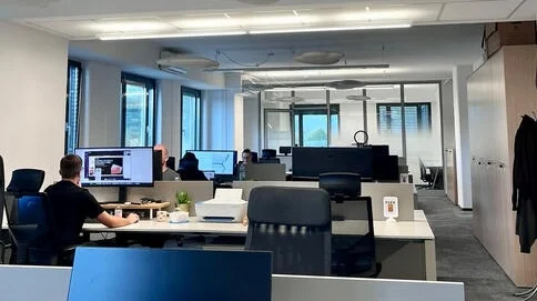 The open-plan floor at Aurora coworking in Ljubljana: standing desks, dual monitors, people working.